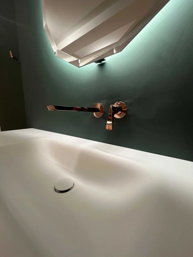 Brassware mounted on dark green wall above white basin